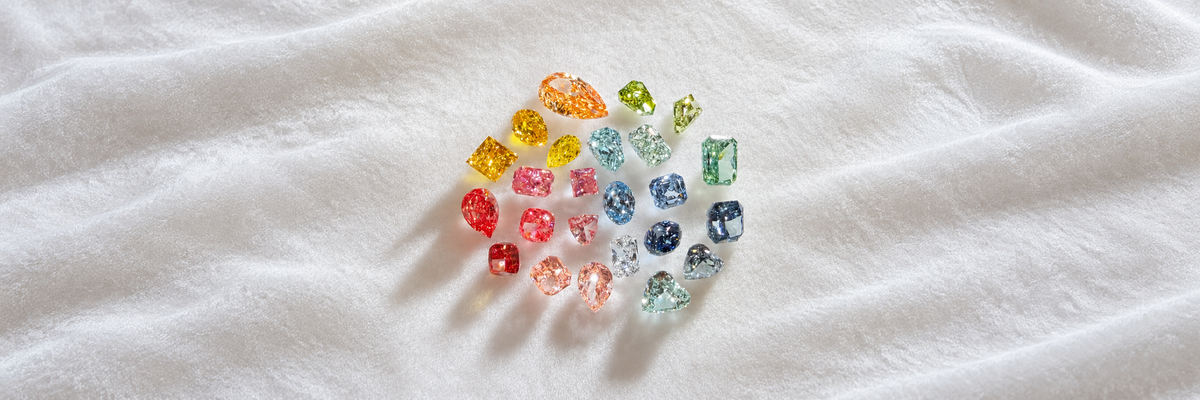 Colourful loose gemstones arranged on softly folded ivory fabric with generous space around the full collection